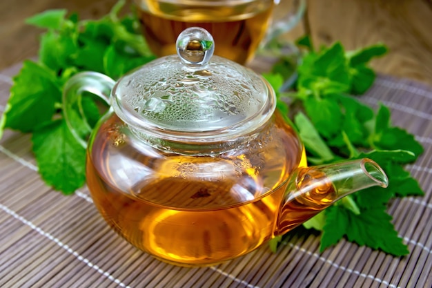 Herbal tea in a glass teapot of fresh mint leaves on bamboo napkin background and wooden board