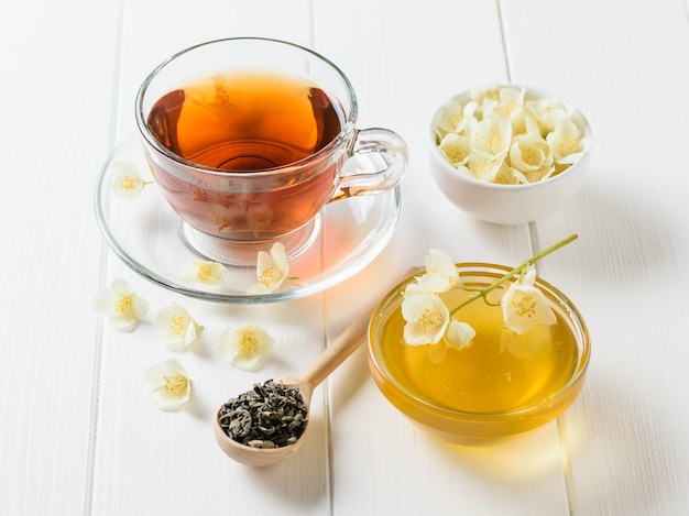 Herbal tea, honey, Jasmine flowers and a wooden spoon on a rustic white table. 