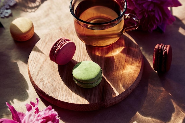 Herbal tea and macarons dessert for brunch Blooming pink peony flowers under trendy hard shadows Relaxation thoughtful meditative good mood lifestyle