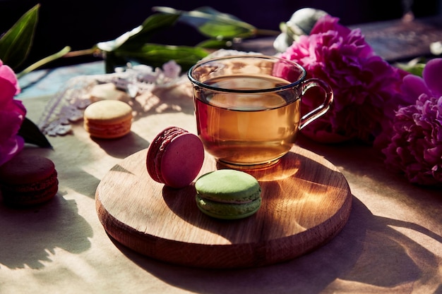 Herbal tea and macarons dessert for brunch outside in the\
terrace blooming pink peony flowers under trendy hard shadows\
relaxation thoughtful meditative good mood lifestyle