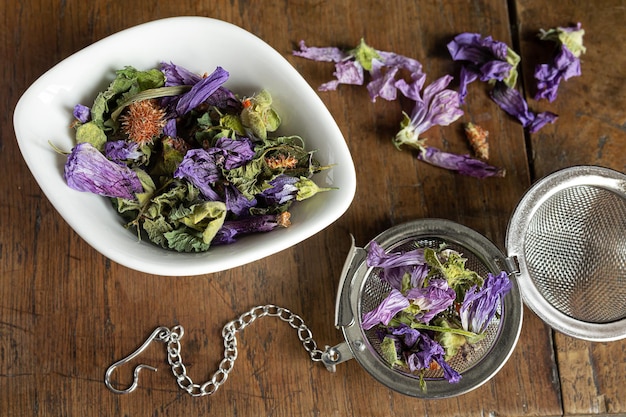 Herbal tea in a white bowl and in a tea infuser on a wooden background top view