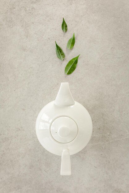 Herbal tea in a white teapot with green tea leaves flat lay top\
view tea concept