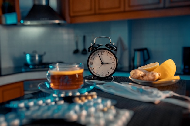レモン、生姜、錠剤とハーブティー。ヘルスケアの概念。目覚まし時計。ぼやけた背景