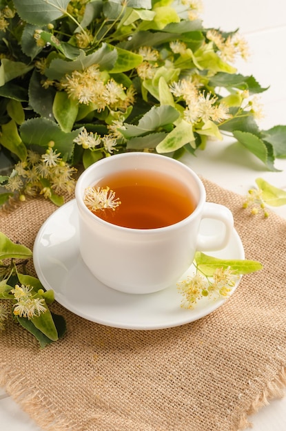 Фото Травяной чай с липовым цветом в белой чашке на белом деревянном столе с цветами