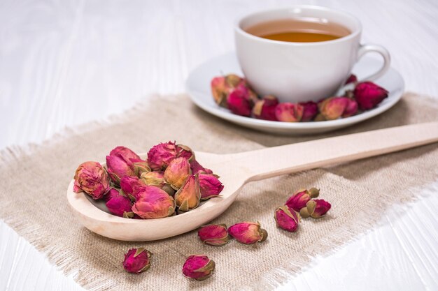 Herbal tea with rosebud White cup with hot tea A wooden spoon with flower buds