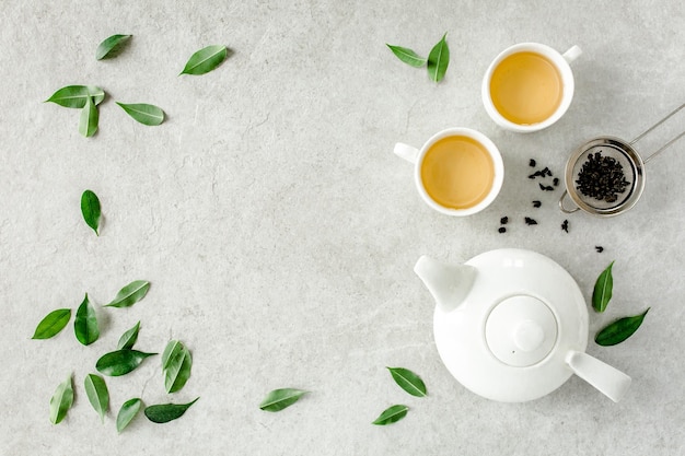 Herbal tea with two white tea cups and teapot with green tea\
leaves flat lay top view tea concept