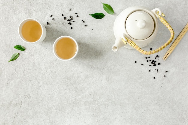 Herbal tea with two white tea cups and teapot with green tea
leaves flat lay top view tea concept