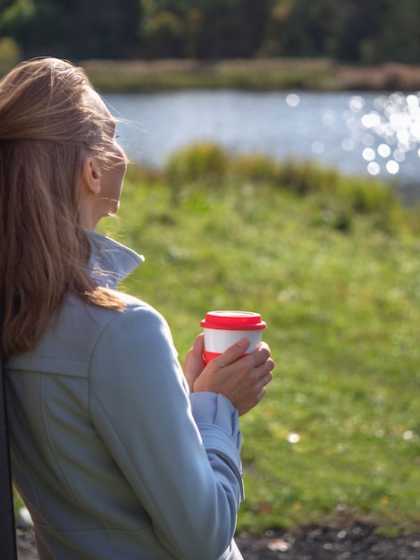 Herbruikbare koffiekopje in de handen van een vrouw in de herfst park.