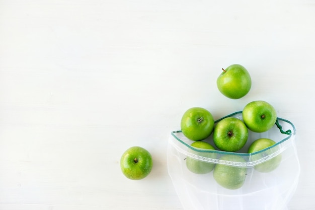 Herbruikbare milieuvriendelijke tas met groene appels op een witte houten ondergrond