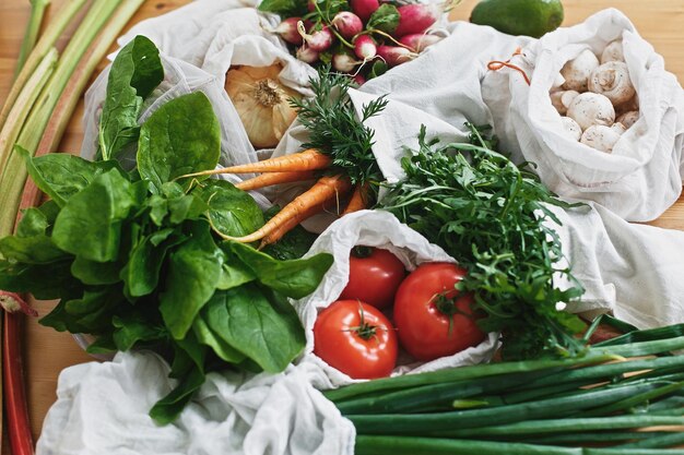 Herbruikbare milieuvriendelijke tassen met verse groenten, wortelen, tomaten, spinazie, rucola, champignons, rhubarbonions op houten tafel, verbod op plastic, Zero waste boodschappenconcept