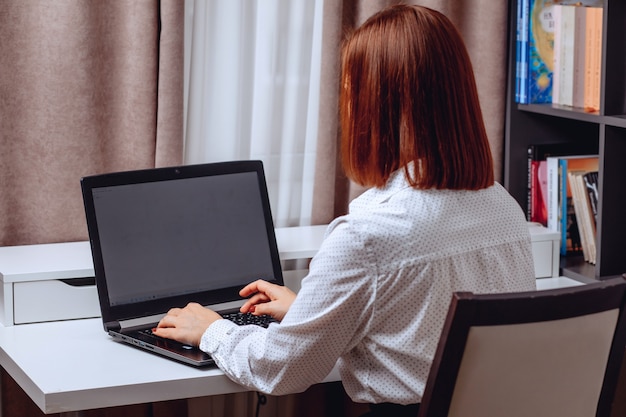 Here can be your advertising. Young girl sitting at the table and looking at the laptop.