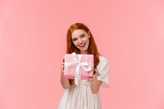 Here you are. Cute and tender, feminine redhead woman giving you her gift, holding wrapped box