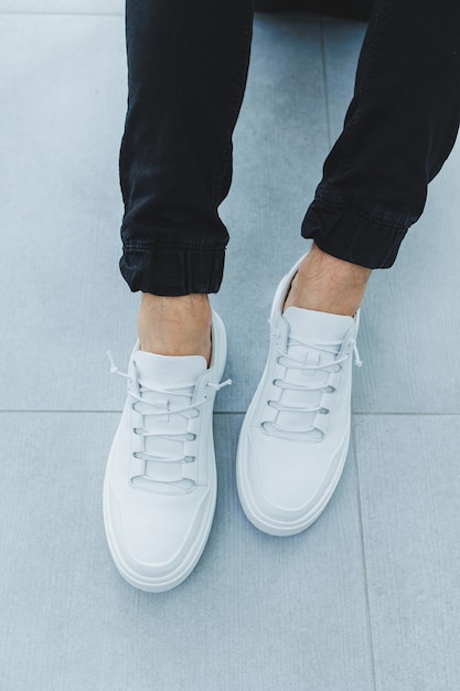 Heren in witte leren casual sneakers met veters en zwarte broek tegen een grijze tegelachtergrond