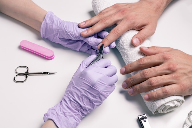 Heren manicure. Schoonheidsspecialist in rubberen handschoenen snijdt nagelriemen op de handen van mannen