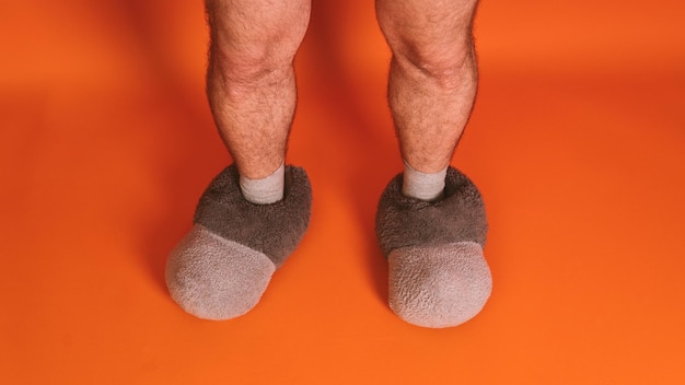 Herenvoeten in sokken en warme grote pantoffels op een oranje achtergrond