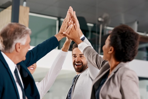 Photo heres to becoming winners shot of a group of businesspeople high fiving together in an office