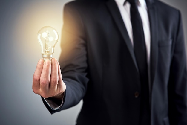 Heres an idea now lets make it happen Cropped studio shot of a businessman holding a glowing lightbulb against a gray background