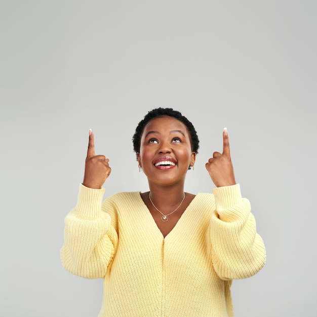 Heres a little something to cheer you up Shot of a young woman pointing at copyspace while posing against a grey background