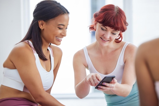 Photo heres that pose i was telling you about. shot of two sporty young women looking at something on a cellphone in a yoga studio.