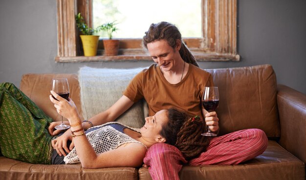 Вот нам любовь Снимок молодой пары с дредами, пьющей вино на диване