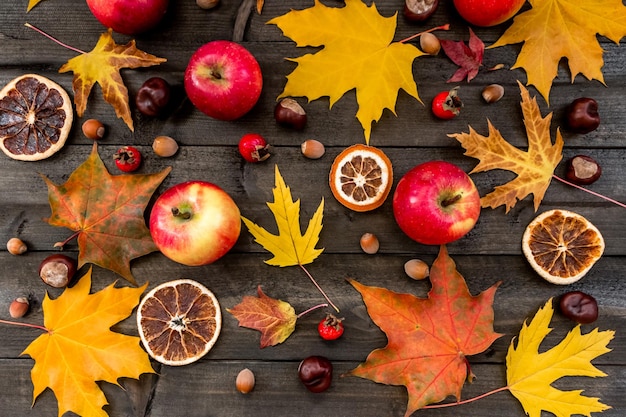 Herfst achtergrond esdoorn bladeren appels rozenbottels noten kastanjes gedroogde sinaasappelen op een houten tafel