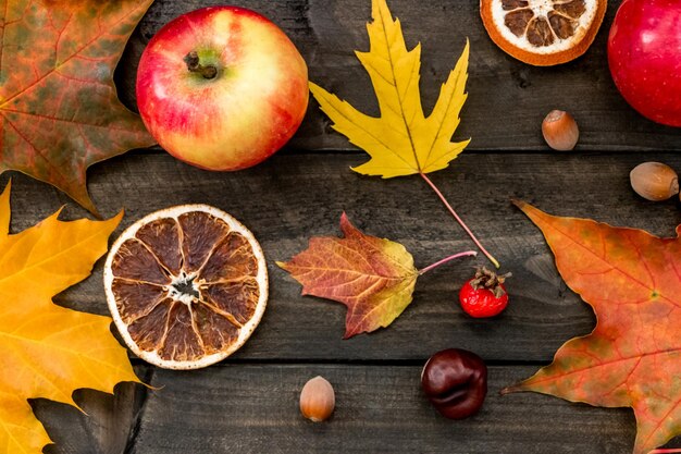 Herfst achtergrond esdoorn bladeren appels rozenbottels noten kastanjes gedroogde sinaasappelen op een houten tafel