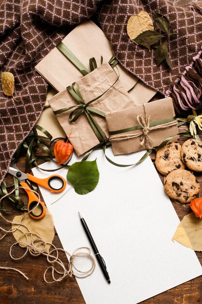 Herfst achtergrond van het voorbereiden van cadeautjes. bovenaanzicht foto van kleine ingepakte cadeaus met chocoladekoekjes, schaar en banden, schoon papier met pen op houten tafel met plaid