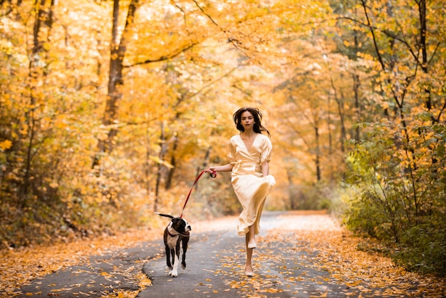 Herfst bos vrouw met hond loopt over een bosweg vrolijk gelukkig jong mooi meisje schoonheid...