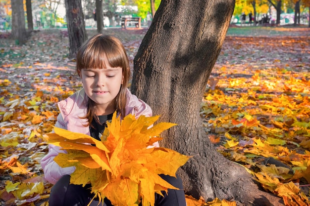 Herfst buitenportret van een kind met een boeket gele esdoornbladeren in een zonnig stadspark