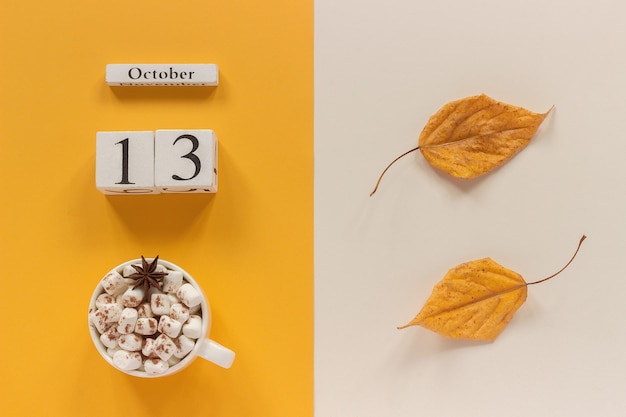 Herfst compositie. Houten kalender 13 oktober, kopje cacao met marshmallows en gele herfstbladeren op gele beige achtergrond. Bovenaanzicht Plat lag Mockup Concept Hallo september.