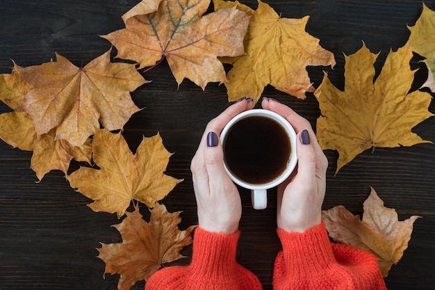 Herfst compositie met platte droge bladeren en koffie in de hand van de vrouw op houten achtergrond. Bovenaanzicht.