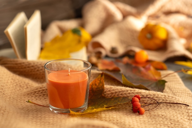 Herfst compositie. Oranje aromakaars op een achtergrond van gevallen bladeren, lijsterbes, een gebreide deken en een open boek.