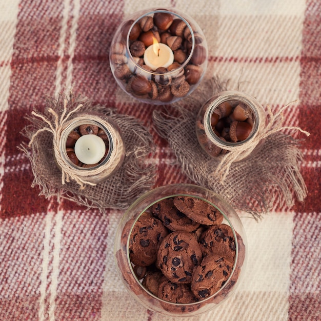 Herfst decoraties. Glazen potten gewikkeld in touwen met eikels, chocoladekoekjes en kaarsen binnen op een bruine plaid.