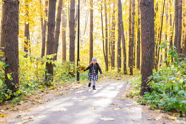 Herfst, geluk en mensen concept - kind loopt door herfstpark met gele bladeren in haar handen.