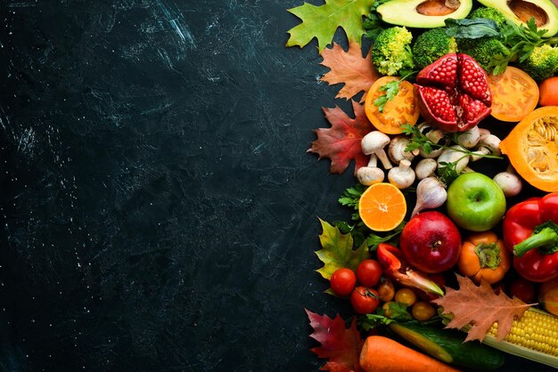 Herfst groenten en fruit op een zwarte stenen achtergrond Pompoen tomaten maïs granaatappel persimmon appel Bovenaanzicht Gratis kopie ruimte