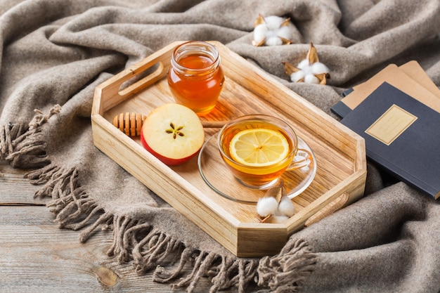 Herfst, herfst, winter interieur in hygge-stijl met drankje. Seizoenssamenstelling met kop hete thee met honing, warme wollen sjaal, zachte plaid op een rustieke houten tafel.