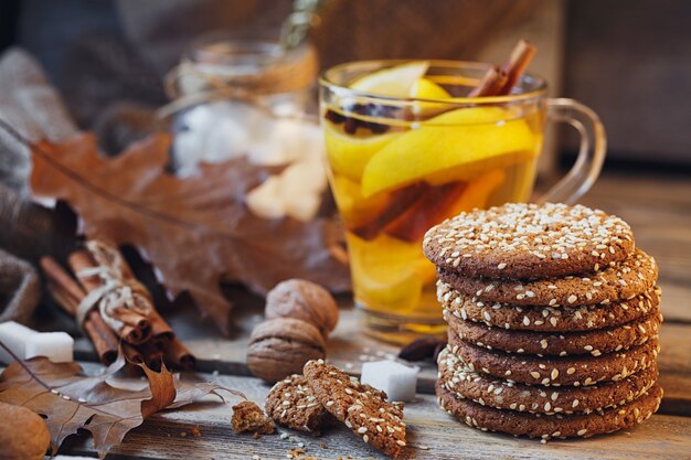 Herfst hete thee met citroen en kruiden in glazen beker. Gezonde thee met koekjes, walnoten en bladeren rond. herfst concept