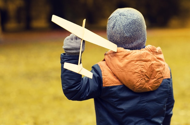 herfst, jeugd, droom, vrije tijd en mensen concept - gelukkig jongetje spelen met houten speelgoedvliegtuig buiten van achteren