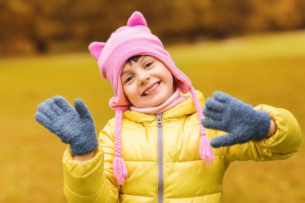 herfst, jeugd, geluk en mensen concept - gelukkig mooi klein meisje zwaaiende handen buitenshuis