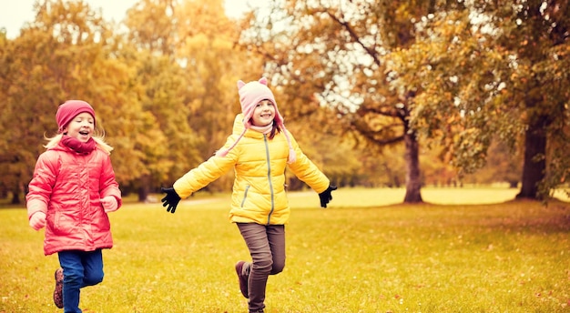 herfst, jeugd, vrije tijd en mensen concept - gelukkige kleine meisjes die tag game spelen en buiten in het park rennen