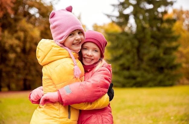 herfst, jeugd, vrije tijd en mensen concept - twee gelukkige kleine meisjes knuffelen in park