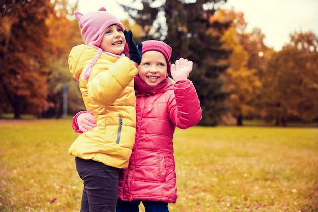 herfst, jeugd, vrije tijd, gebaar en mensenconcept - gelukkige kleine meisjes zwaaiende handen in het park buiten