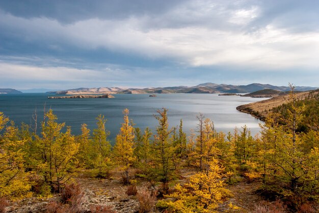 Herfst landschap met bomen en uitzicht op het Baikalmeer, gele bomen op de voorgrond en wolken aan de hemel