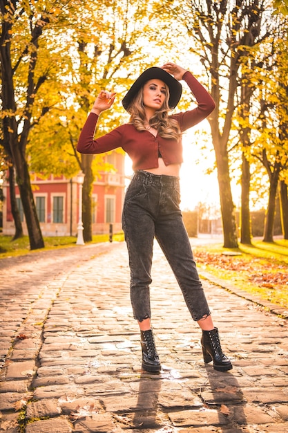 Herfst levensstijl bij zonsondergang blonde blanke vrouw in een rode trui en zwarte hoed genieten van de natuur in een park met bomen