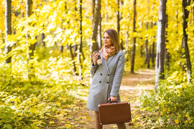 Herfst, natuur en mensen concept - Jonge mooie vrouw in grijze jas met een kopje koffie