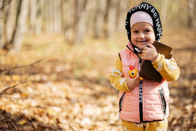 Herfst openluchtportret van mooi gelukkig babymeisje in bos met spechtstuk speelgoed in handen