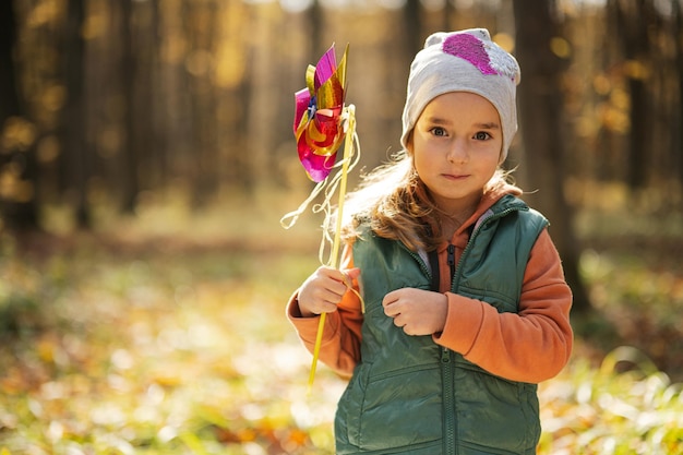 Herfst openluchtportret van mooi gelukkig kindmeisje in bos met windmolenstok