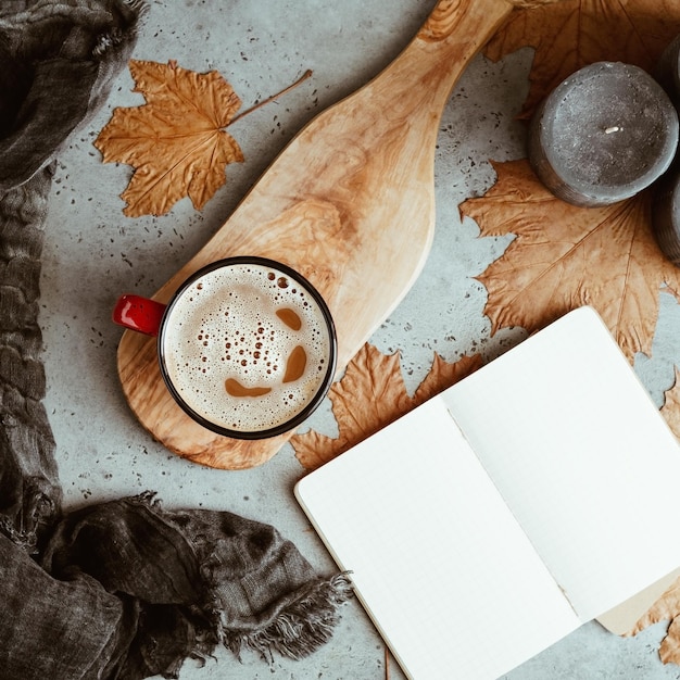 Herfst plat lag compositie op een grijze betonnen achtergrond Esdoorn verlaat het open notitieboekje met lege vellen koffie zwarte aromatische kaarsen en warme sjaal Mockup bovenaanzicht