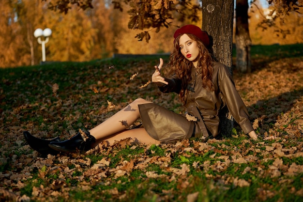 Herfst portret van een vrouw in een hoed baret en regenjas in de buurt van een boom in de herfst geel gebladerte