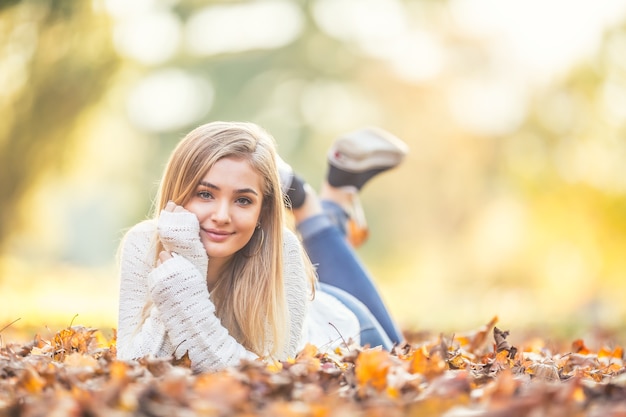 Herfst portret van jonge vrouw liggend op esdoorn bladeren in park.